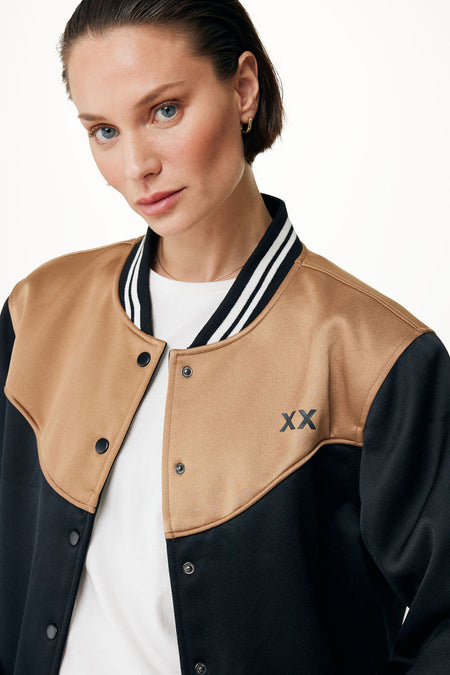 Manteau court noir de MEXX, avec des accents caramel et les lettres XX, porté sur un chemisier blanc.