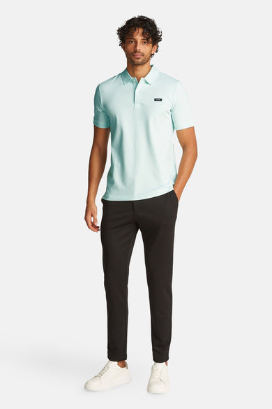 Polo vert de Calvin Klein avec des manches courtes, porté avec un pantalon noir et des chaussures blanches.