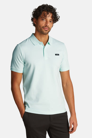 Polo vert clair avec manches courtes de Calvin Klein, porté avec un pantalon noir.