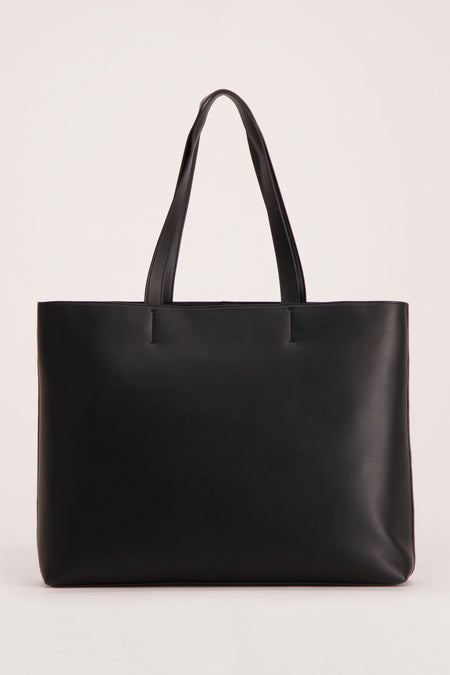 Sac à main noir de Calvin Klein, avec des bretelles, contre un léger fond.