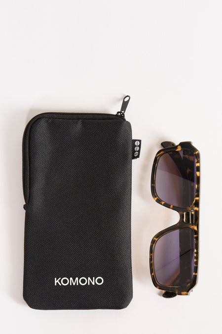 Lunettes vertes de KOMONO, à côté d'un étui de protection noir avec le logo de la marque.