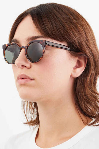 Lunettes de soleil jaune-brun de KOMONO, portées par un modèle aux cheveux bruns et à un T-shirt blanc.