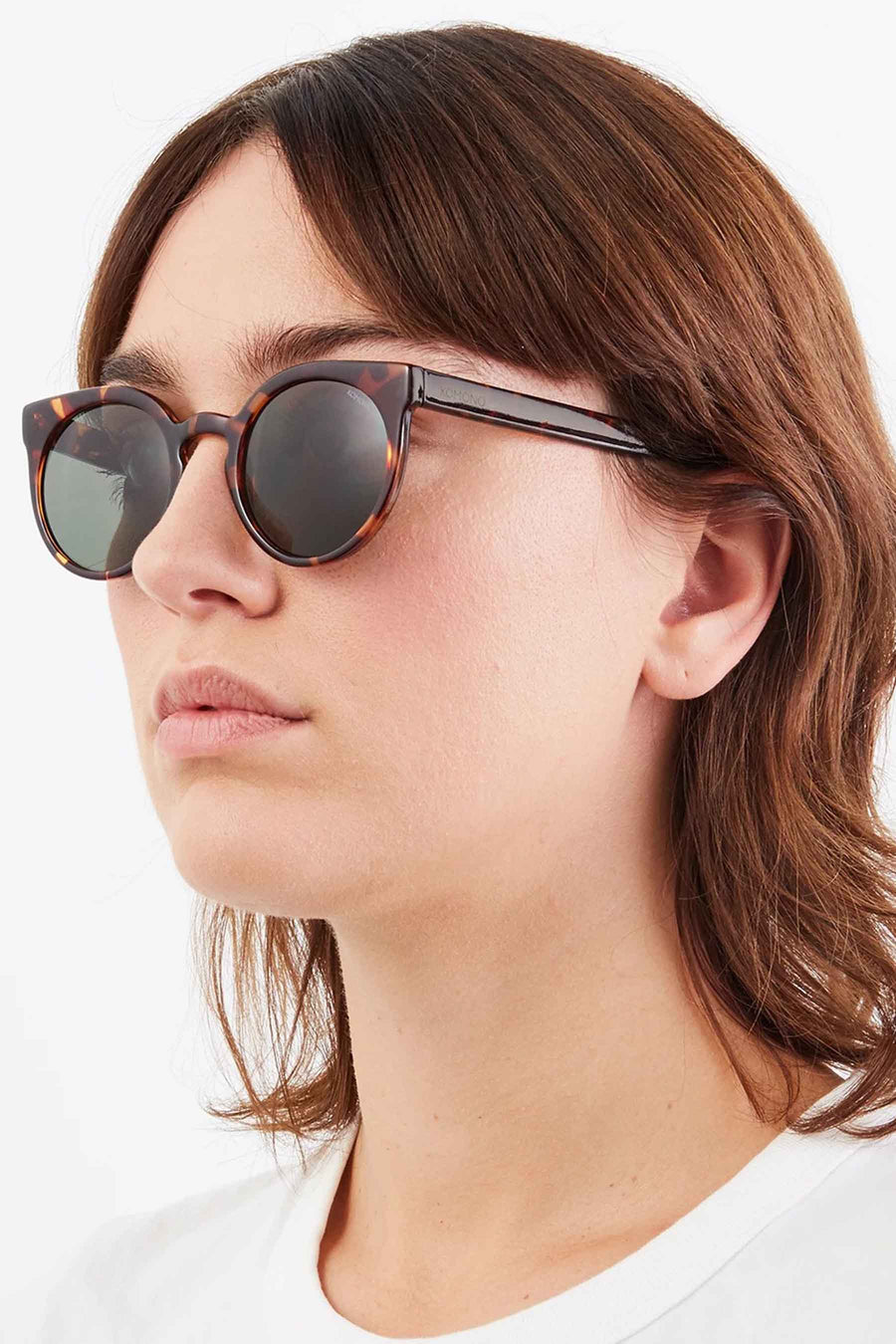 Lunettes de soleil jaune-brun de KOMONO, portées par un modèle aux cheveux bruns et à un T-shirt blanc.