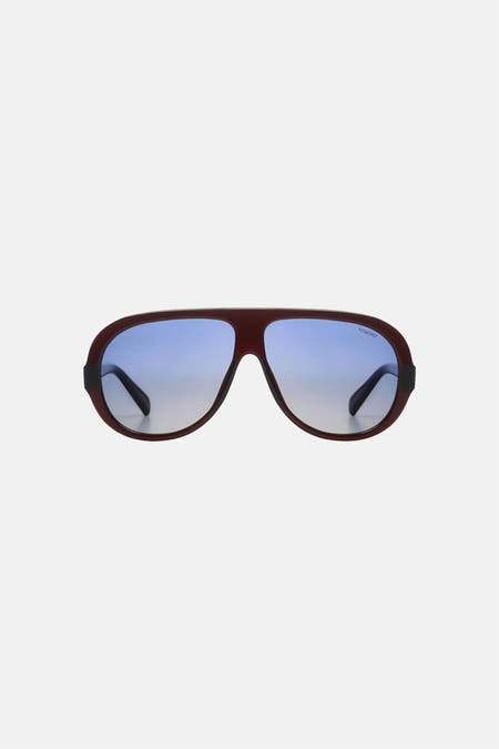 Lunettes rouge-brun de KOMONO avec verres à dégradé bleu et logo.