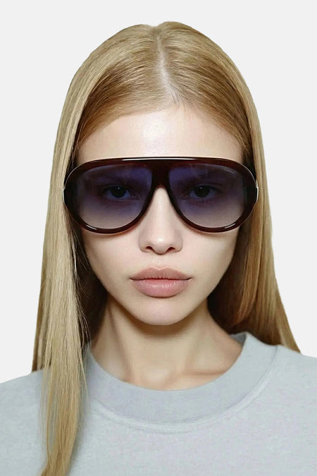 Lunettes de soleil bordeaux de KOMONO avec verres foncés, portées par un mannequin aux cheveux blonds et portant un pull gris clair.