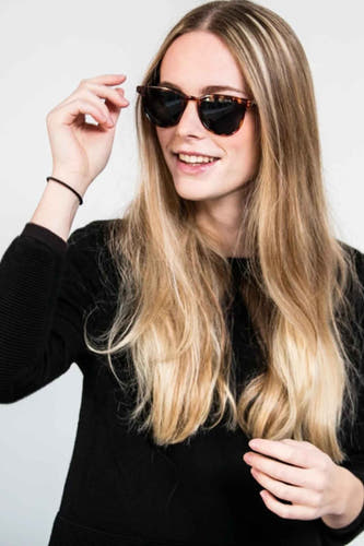 Lunettes de soleil vertes de KOMONO, portées par une femme aux longs cheveux blonds et à un pull noir.