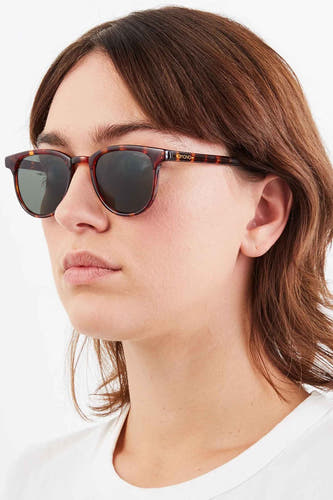 Lunettes de soleil vertes de KOMONO, avec un motif tortue et portées par une femme aux cheveux bruns.