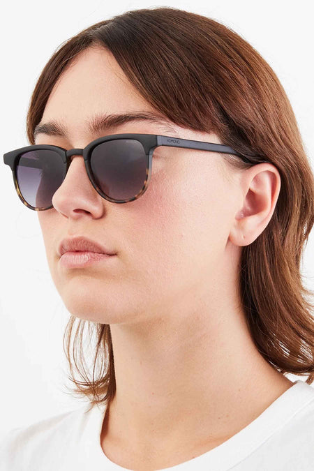 Lunettes de soleil noires KOMONO, avec un motif subtil de tortue à la base du montant.