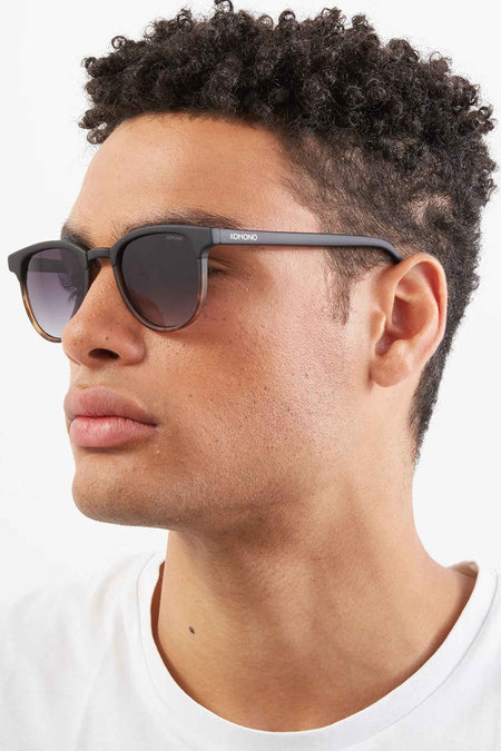 Lunettes de soleil noires KOMONO, vues en profil sur un modèle portant un T-shirt blanc.