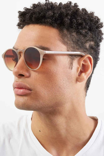 Lunettes de soleil beige de KOMONO, portées par une personne en vue latérale.