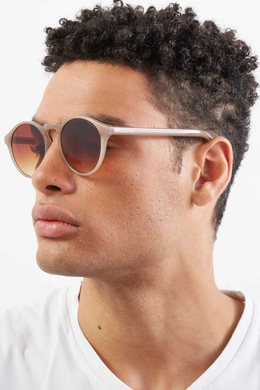 Lunettes de soleil beige de KOMONO, portées par une personne en vue latérale.