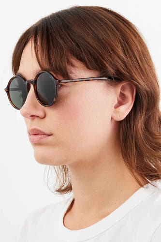 Lunettes de soleil vertes de KOMONO, avec un cadre tacheté, portées par une femme en un T-shirt blanc.