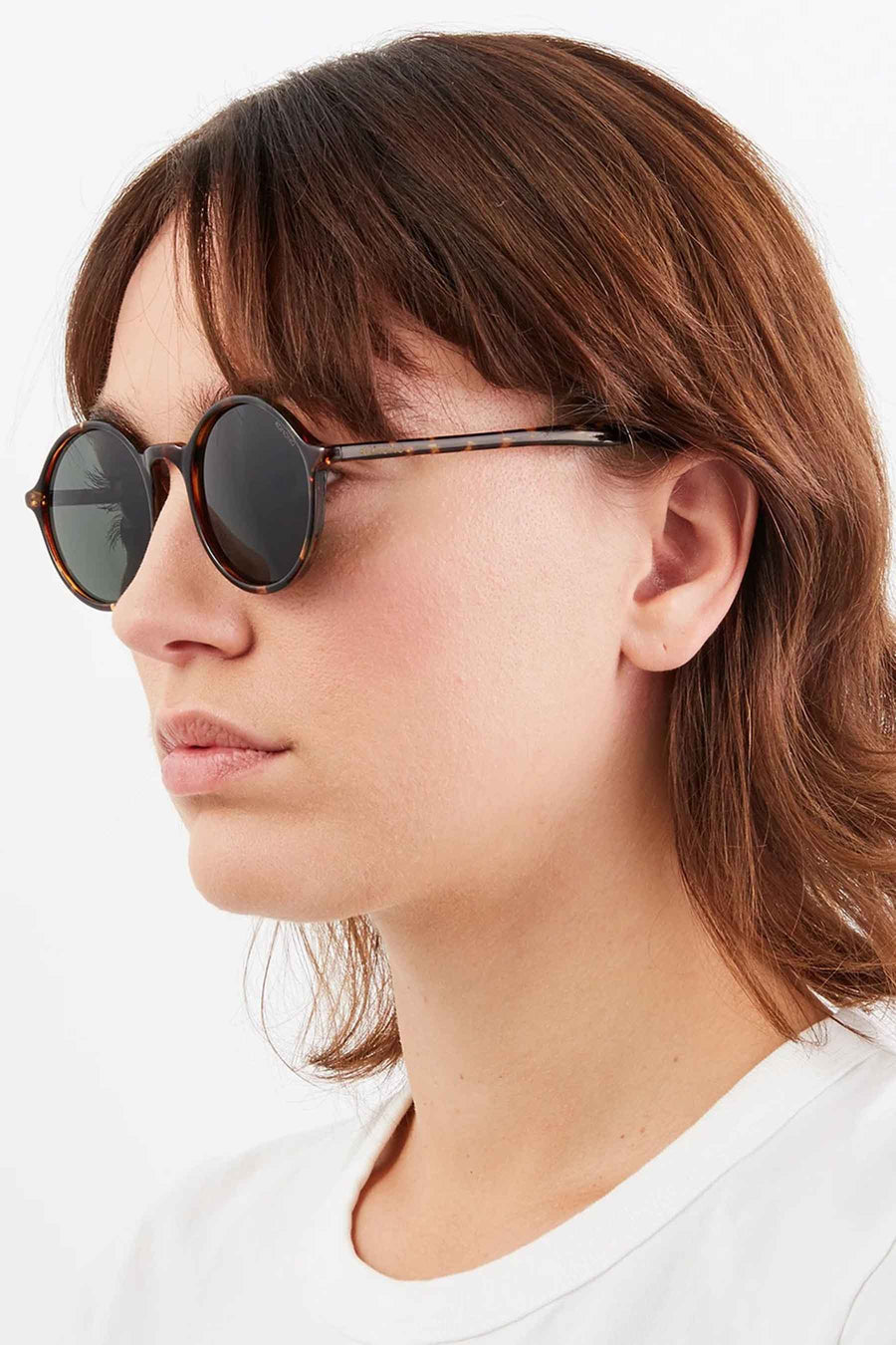 Lunettes de soleil vertes de KOMONO, avec un cadre tacheté, portées par une femme en un T-shirt blanc.