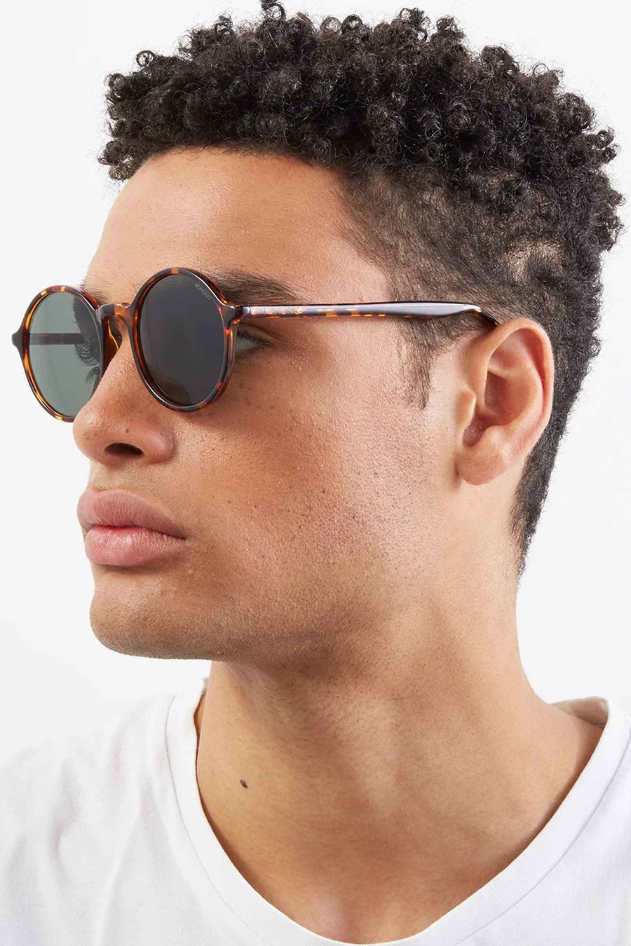 Lunettes de soleil vertes de KOMONO, avec un cadre en tortue, portées par un homme avec un t-shirt blanc.
