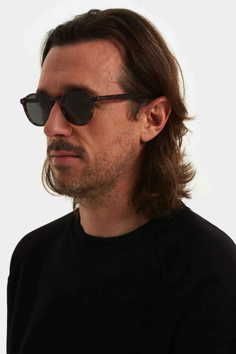 Lunettes de soleil brunes de KOMONO, avec une impression tachetée et portées par un homme en chemise noire.