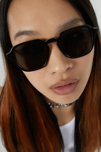 Lunettes de soleil noires de KOMONO, portées avec une chaîne de couleurs argentées et un t-shirt blanc.