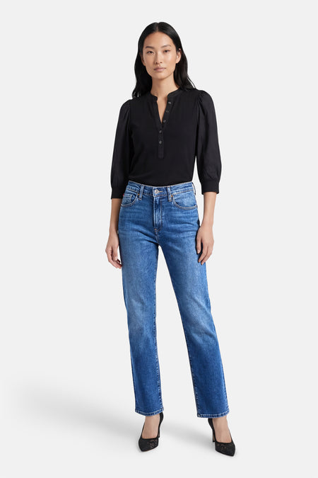 Rechte jeans van middenblauw denim van Lee Cooper, met hoge taille en gedragen met een zwarte blouse en zwarte schoenen.