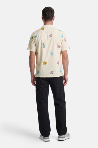 Creme short-sleeved hemd van LAKOR met kleurrijke koraalprint, gezien van achteren, gedragen door een man met zwarte broek en grijze sneakers.