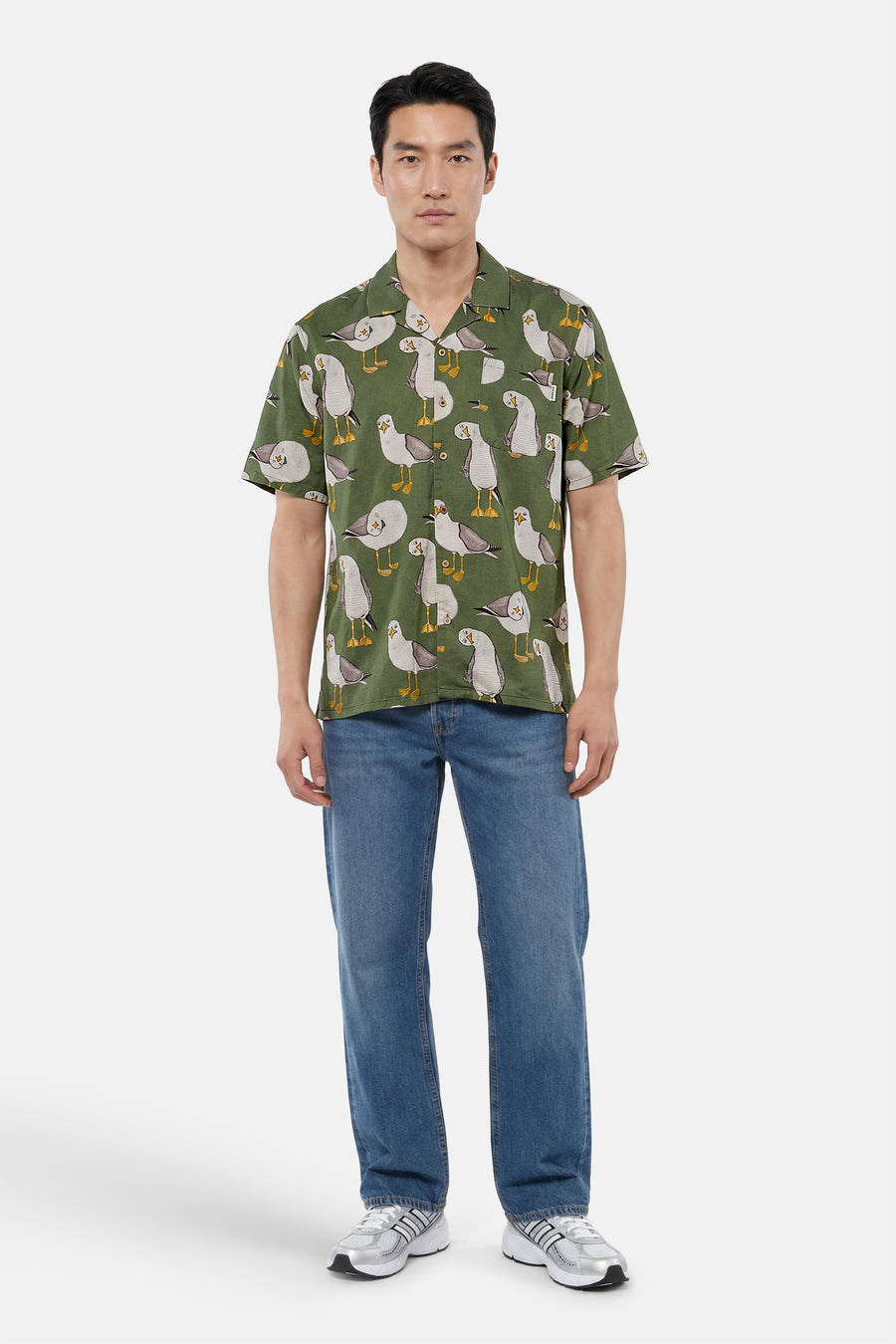 Chemise verte à manches courtes de LAKOR avec imprimé mouettes, portée par un homme avec un jean bleu et des baskets argentées.