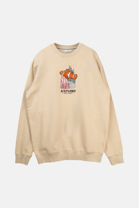 Pull écru de LAKOR, vu de dos, à manches longues et associé à un short vert et une casquette.
