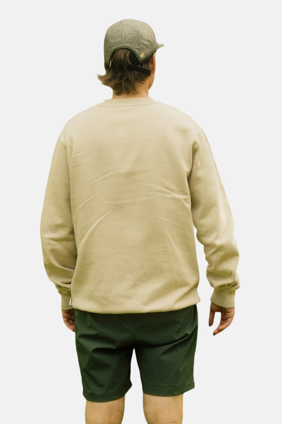 Ecru sweater van LAKOR, gezien van achteren, met lange mouwen en gecombineerd met groene shorts en een pet.
