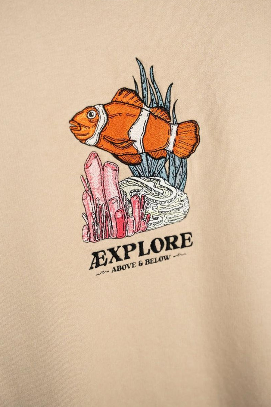 Pull écru à col rond de LAKOR, avec une image brodée d'un poisson-clown et le texte "EXPLORE".