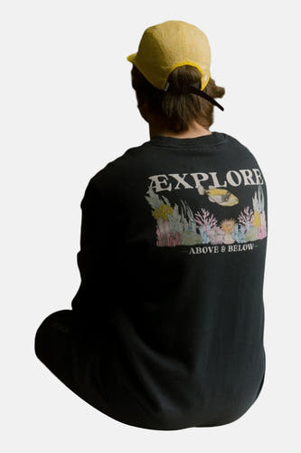 Zwarte sweater van LAKOR, met een print van koraalriffen en de tekst "Explore Above & Below" op de rug, met een gele pet.

