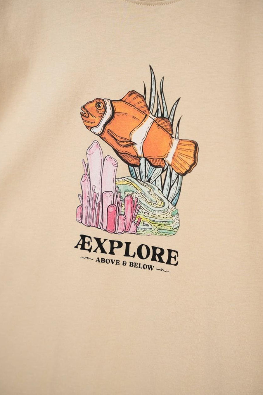 T-shirt beige de LAKOR avec imprimé de poisson-clown, corail et le texte "Explore Above & Below".