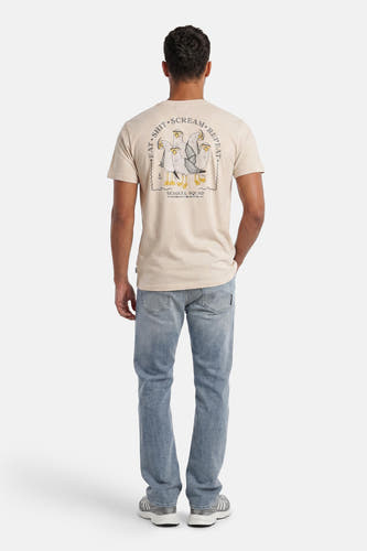 Ecru T-shirt van LAKOR met een 'Seagull Squad' print op de achterkant, gedragen door een model in jeans en sneakers.
