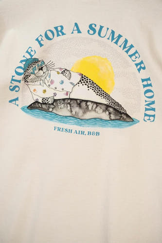 Ecru T-shirt van LAKOR met een grafische print van een zeehond op een steen voor een zomerhuis.