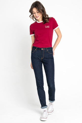 Femme en T-shirt rouge Lee, jeans bleu marine et baskets Converse blanches, debout.