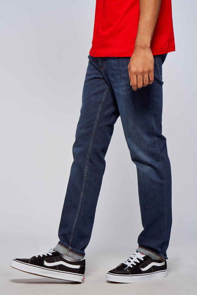 Jean droit bleu marine de Lee Cooper, avec poche visible et sneakers à rayures.