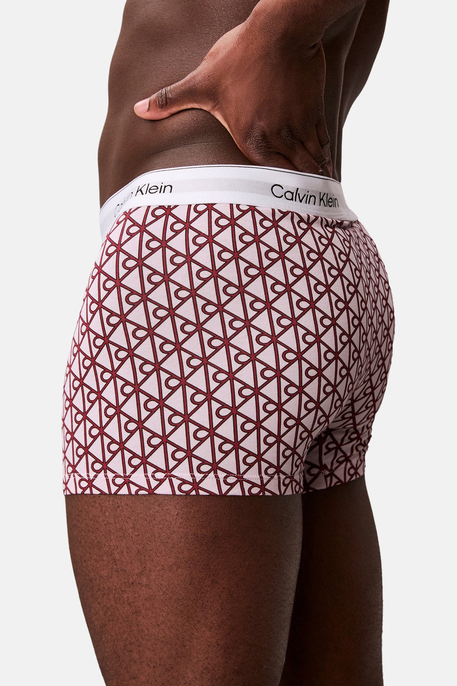 Boxer Calvin Klein rose clair avec motif géométrique rouge foncé et ceinture blanche, vue de côté et de dos.