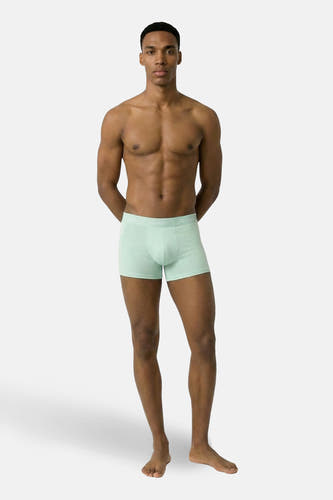 Slip Calvin Klein verte, porté par un homme musclé à la peau foncée, les mains dans le dos.