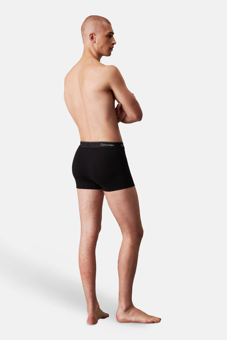 Boxer noir Calvin Klein porté par un homme, debout de profil avec les bras croisés, avec ceinture logo visible.