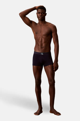 Zwarte boxershort van Calvin Klein, gedragen door een mannelijk model met een ontbloot bovenlichaam, staand tegen een witte achtergrond.