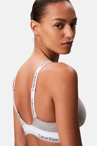 Soutien-gorge gris Calvin Klein, avec bretelles blanches à logo, vu de dos par-dessus l'épaule.