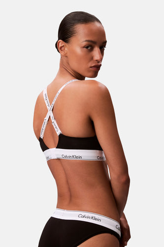 Vrouw in zwarte Calvin Klein lingerie met witte banden, over de schouder kijkend.