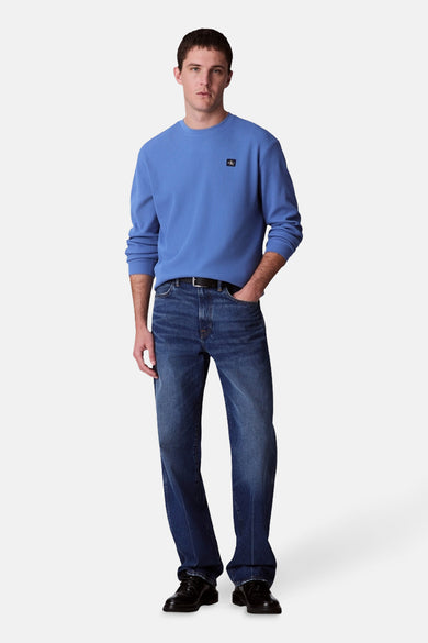 T-shirt bleu à manches longues de Calvin Klein, porté avec un jeans foncé et des chaussures en cuir noir.