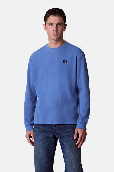 T-shirt bleu à manches longues de Calvin Klein, porté avec des jeans foncés et des chaussures noires, dos.