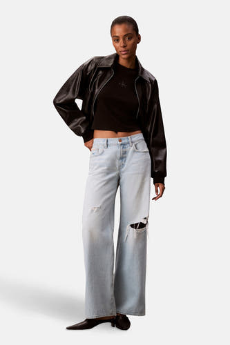 T-shirt noir à manches longues de Calvin Klein, porté sous une veste en cuir noire et des jeans larges déchirés.