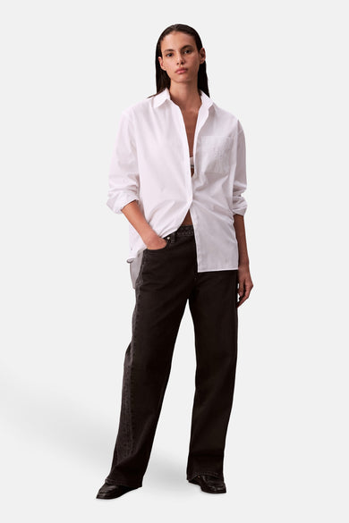 Chemise blanche à manches longues de Calvin Klein, portée avec des jeans noirs et des chaussures foncées.