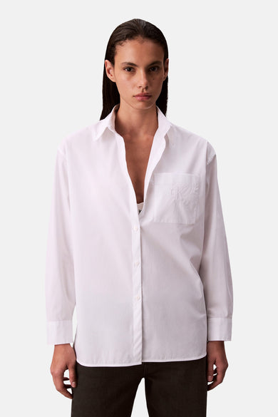 Chemise blanche à longues manches de Calvin Klein, avec poche poitrine et portée avec une chemise blanche.