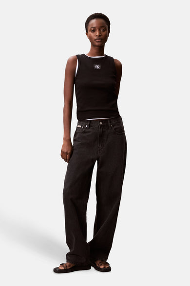 T-shirt noir de Calvin Klein avec un logo blanc sur la poitrine et porté avec des jeans larges et sombres.