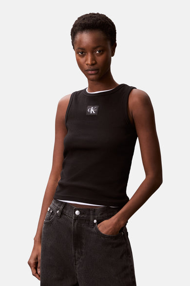 T-shirt noir Calvin Klein, avec texture côtelée et logo sur la poitrine, porté avec un pantalon de travail foncé.