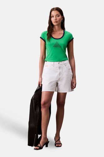 T-shirt vert avec manches courtes de Calvin Klein, avec une impression de texte noire et porté avec un short blanc et des sandales noires.