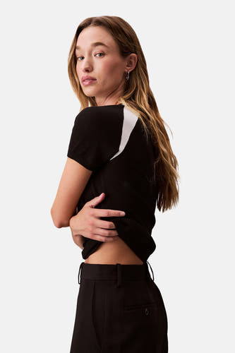 T-shirt noir à manches courtes de Calvin Klein, avec une bande blanche sur l'épaule, porté avec un pantalon noir.