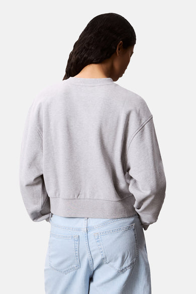 Pull-over gris à col rond de Calvin Klein, avec une longueur cropped et des jeans légers.