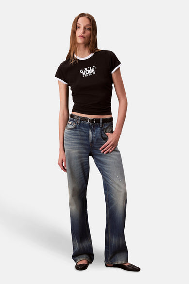 T-shirt noir à manches courtes de Calvin Klein, avec une patte blanche le long de la ligne du col, porté avec un jean et des chaussures noires.