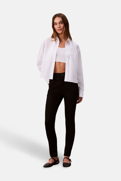 Jean skinny noir de Calvin Klein, associé à un crop top blanc et une chemise blanche déboutonnée.